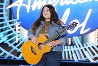 a woman holding an acoustic guitar on the american idol stage
